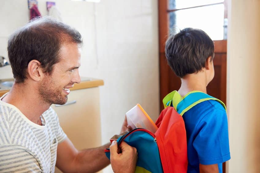 Father helping his son pack his school bag.