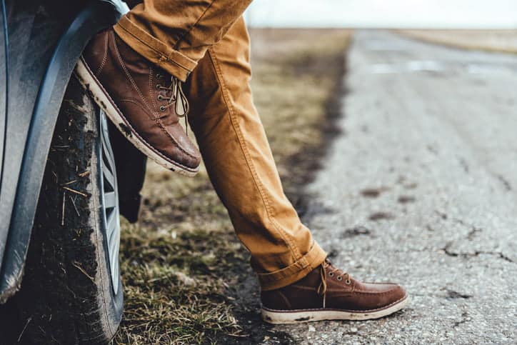 man leaning against his car with his foot on the wheel