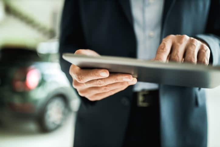 Close up of unrecognizable salesperson using touchpad in a car showroom.