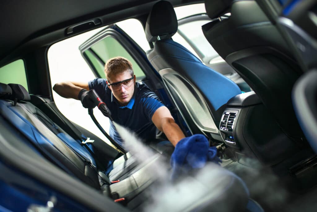 Closeup side view of a young man using fine brush and cleaning AC vents during car interior detailed cleaning.