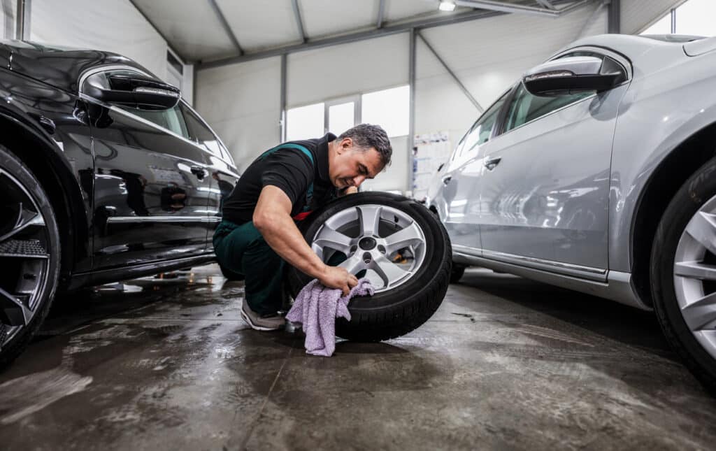 Professional car service worker polishing luxury car rim with microfiber rag or cloth in a car detailing and valeting shop.