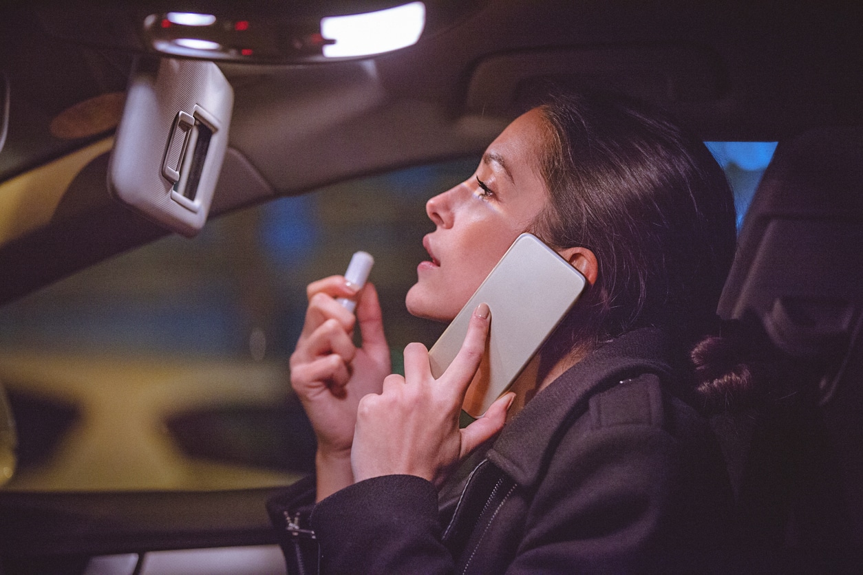 Female on the phone whilst looking in the interior mirror of a car