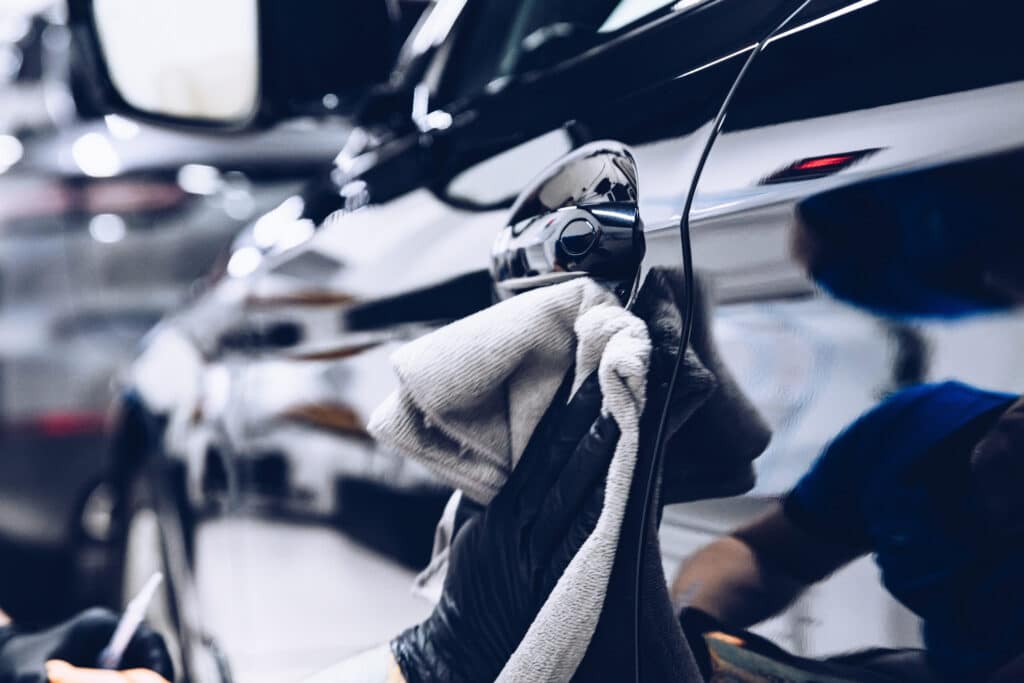 Car mechanic wiping black car with a grey cloth