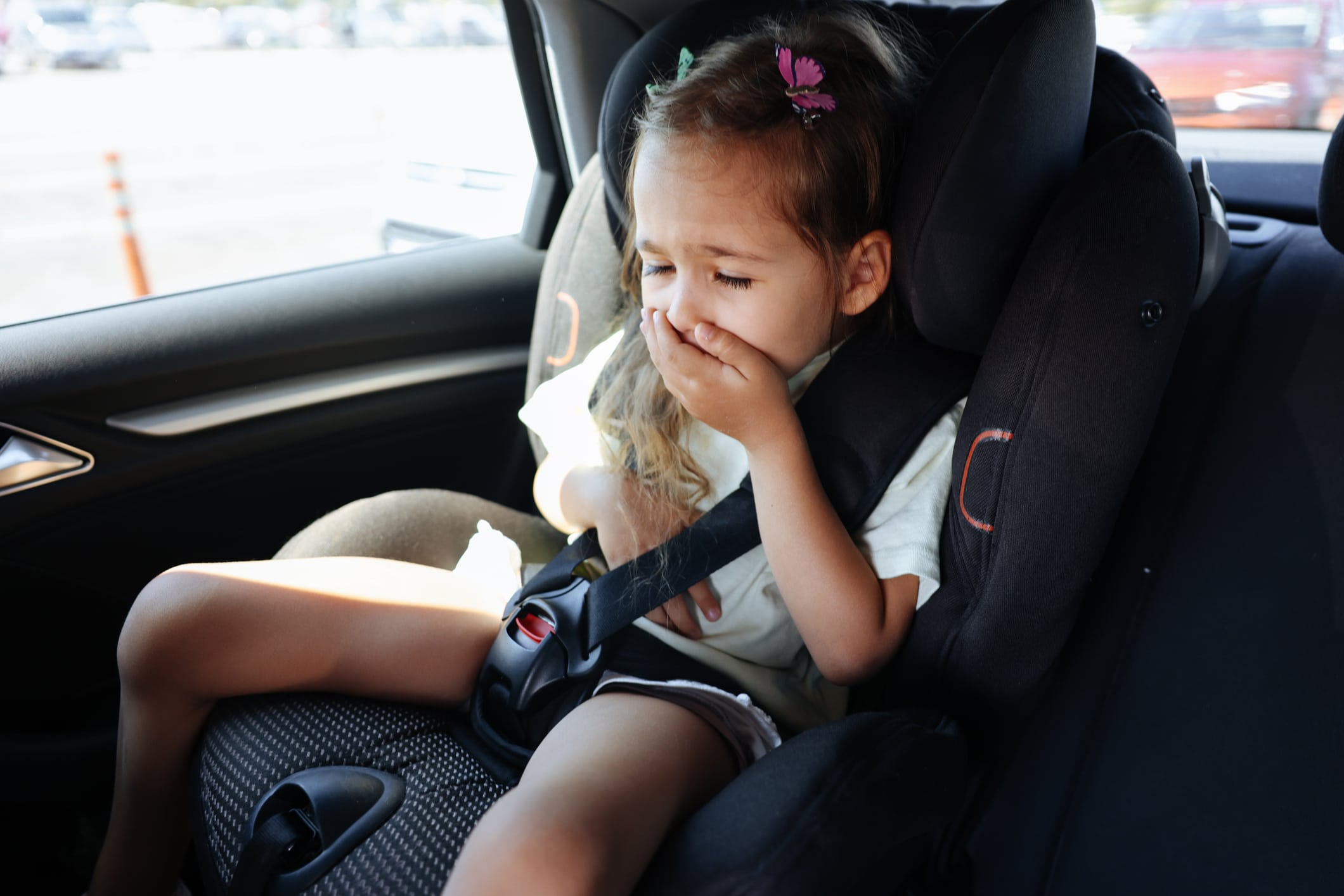 Small female child in car seat covering mouth with hand