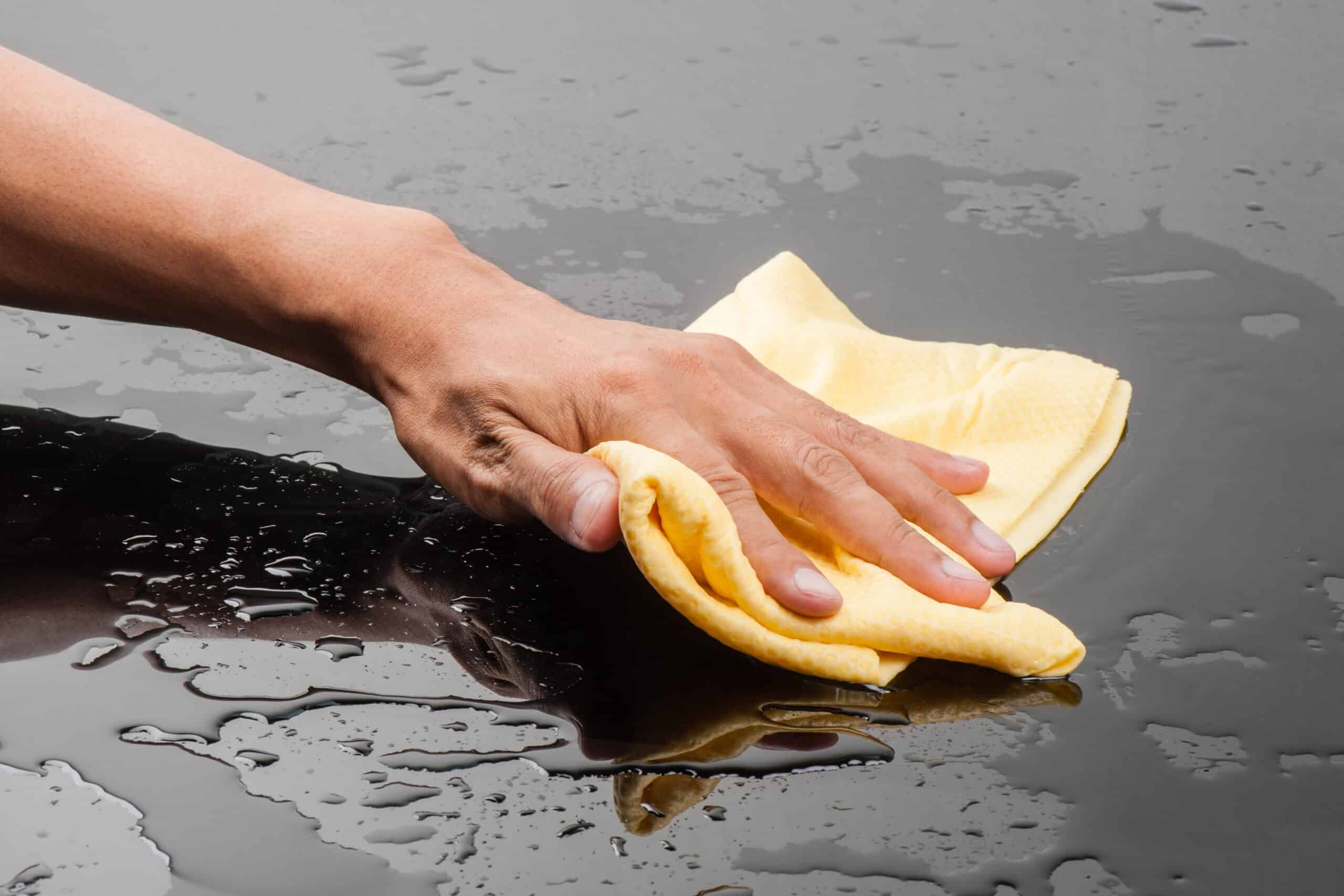 Cropped image of a males hands drying a wet black car surface with a yellow cloth