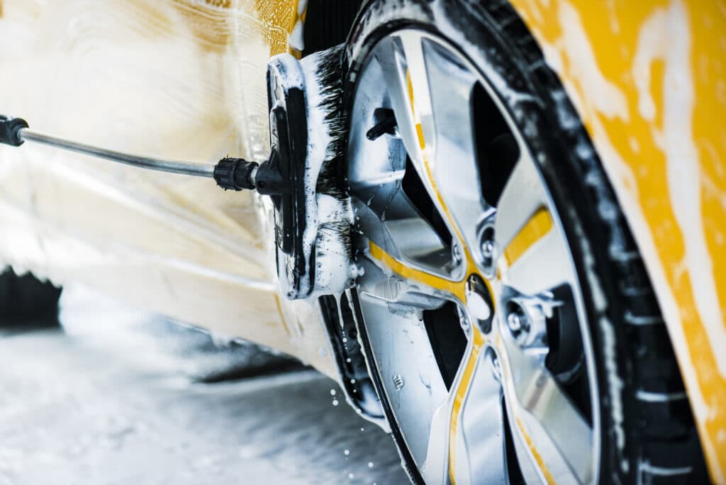 Man washing a car using brush and soap or foam. Manual cleaning modern aloy wheel in selective focus.