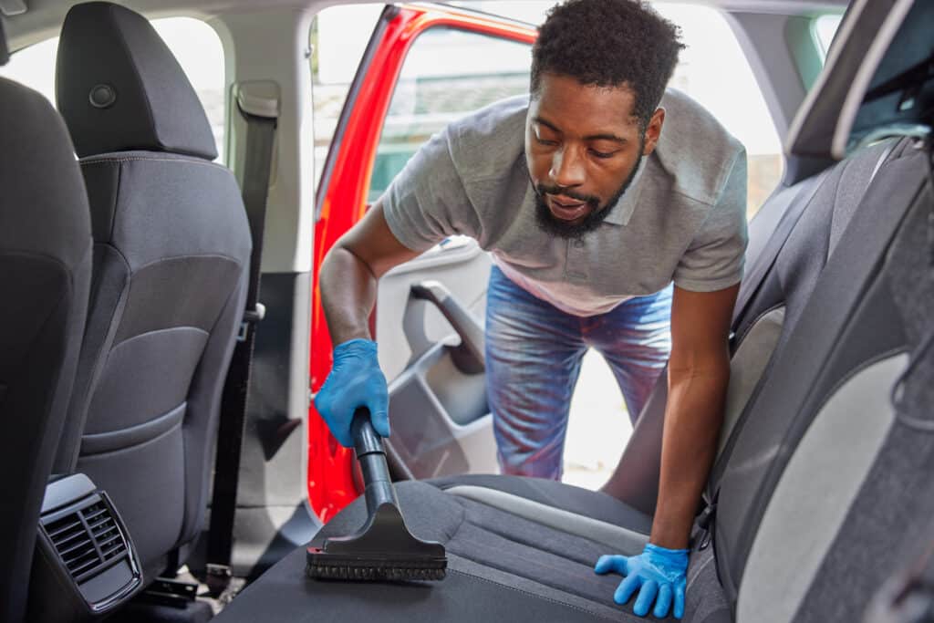 Man Hoovering  And Cleaning Rear Seats Of Car During Car Valet