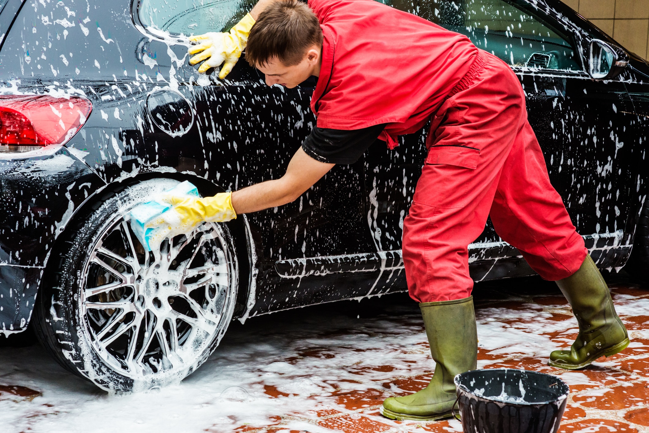 Male worker at car wash service washing the car tire.